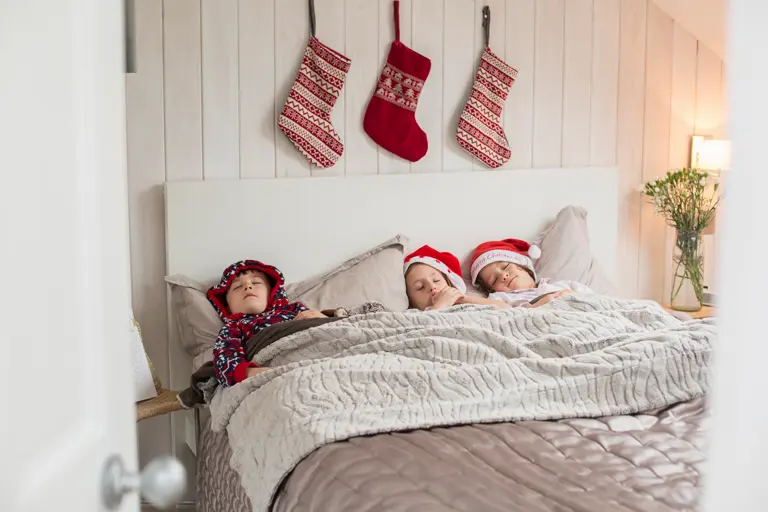 Christmas stockings on the wall above the bed of three sleeping children.