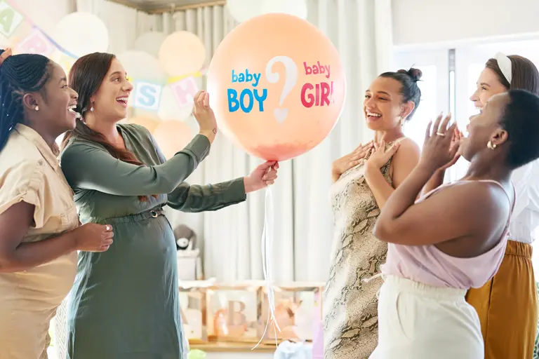 Women at a gender reveal party getting ready to pop a gender reveal balloon.