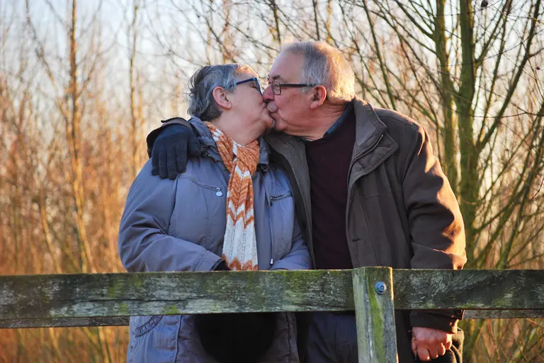 Older couple kissing on a bridge.